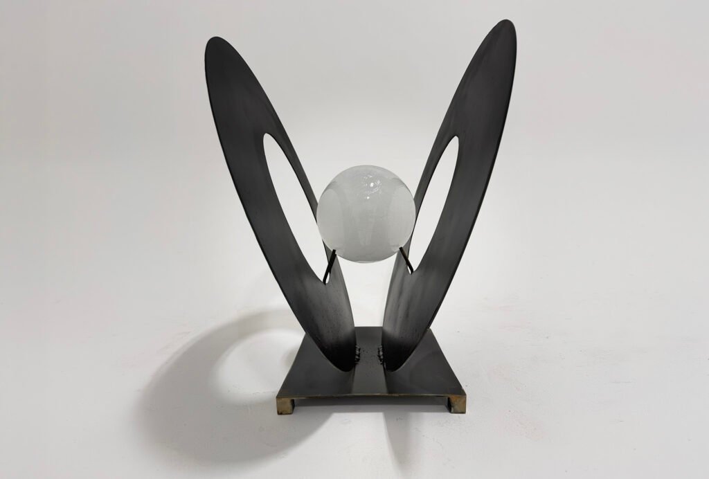Drawn Together by Marisa Mitchell by Marisa Mitchell with two curved black forms surrounding a glass sphere
